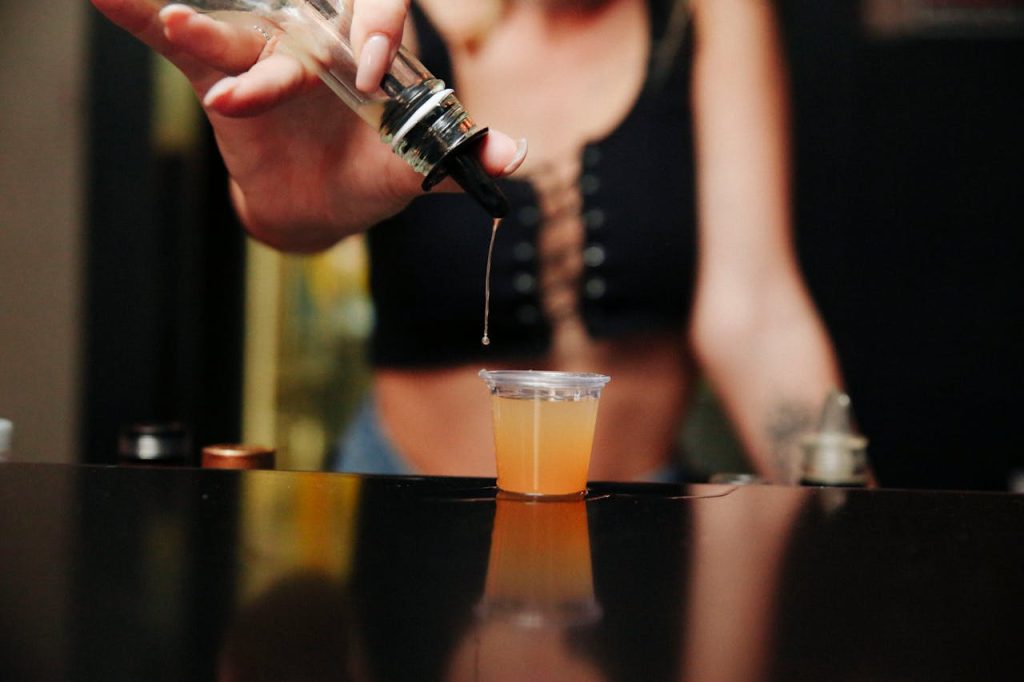 A bartender pouring a beverage into a shot glass with focus on the liquid and hands.